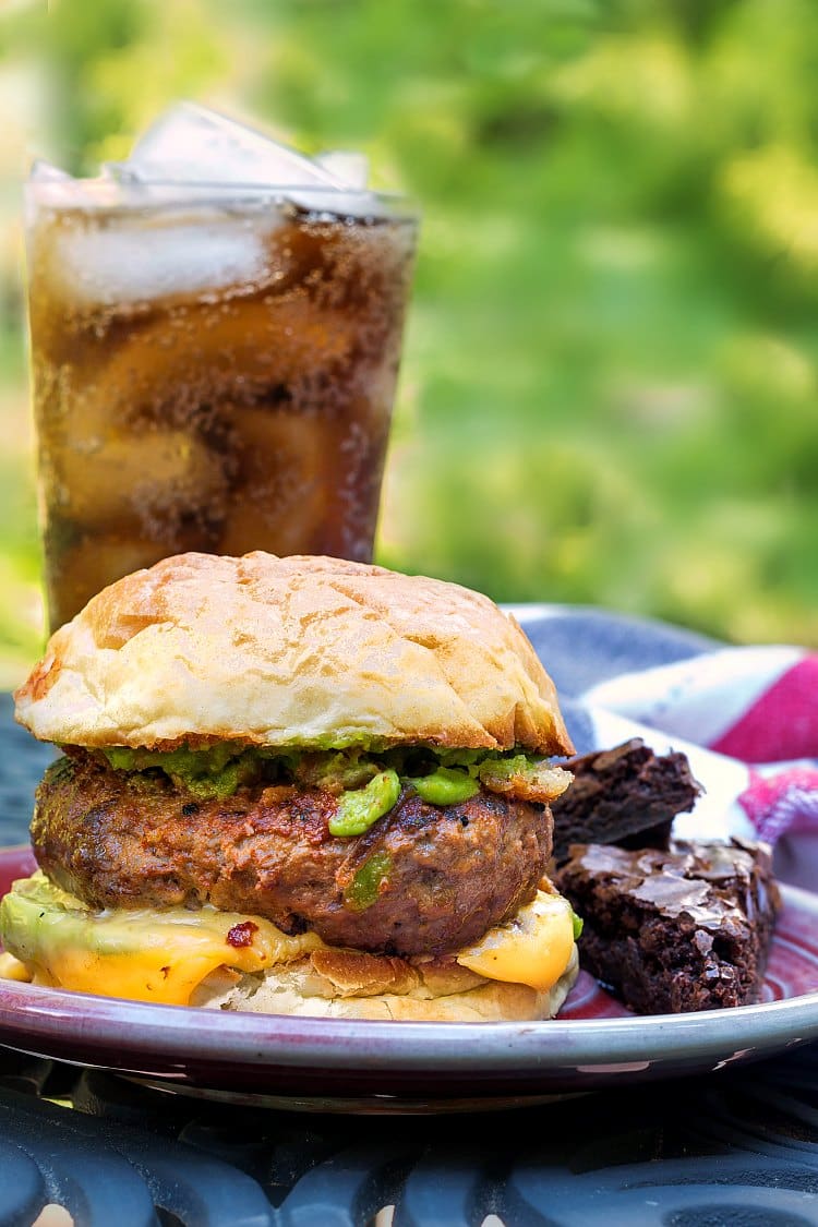 A thick meaty burger on a bun with a brownie and a glass of Coke. 