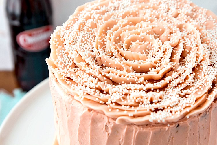 Overhead shot of a pink iced cake with a rose decoration on top and white sprinkles.