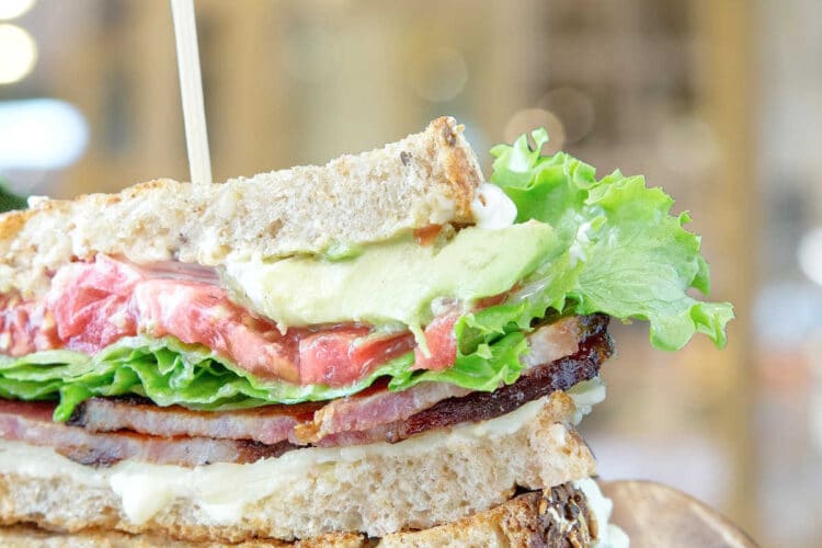 A blt sandwich cut and stacked on a wooden plate.