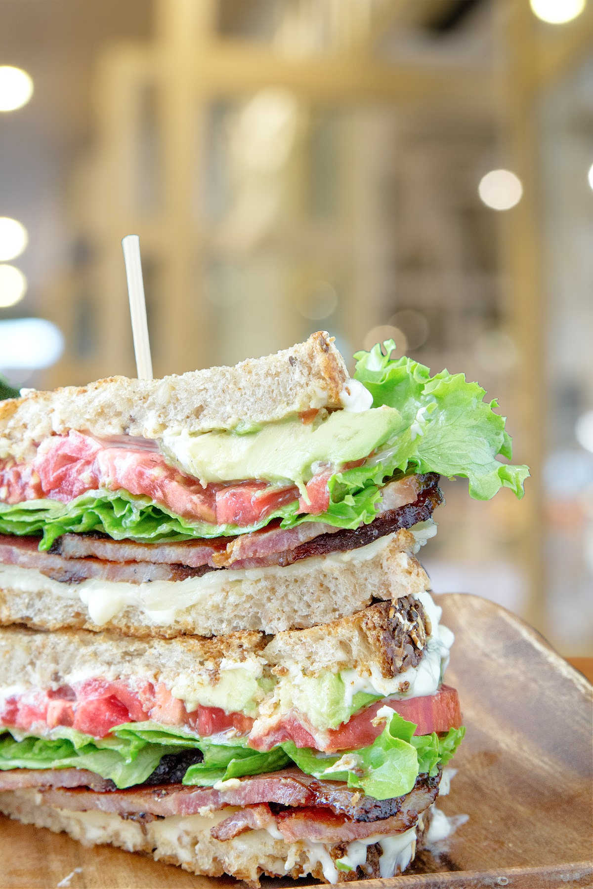 A blt sandwich cut and stacked on a wooden plate.