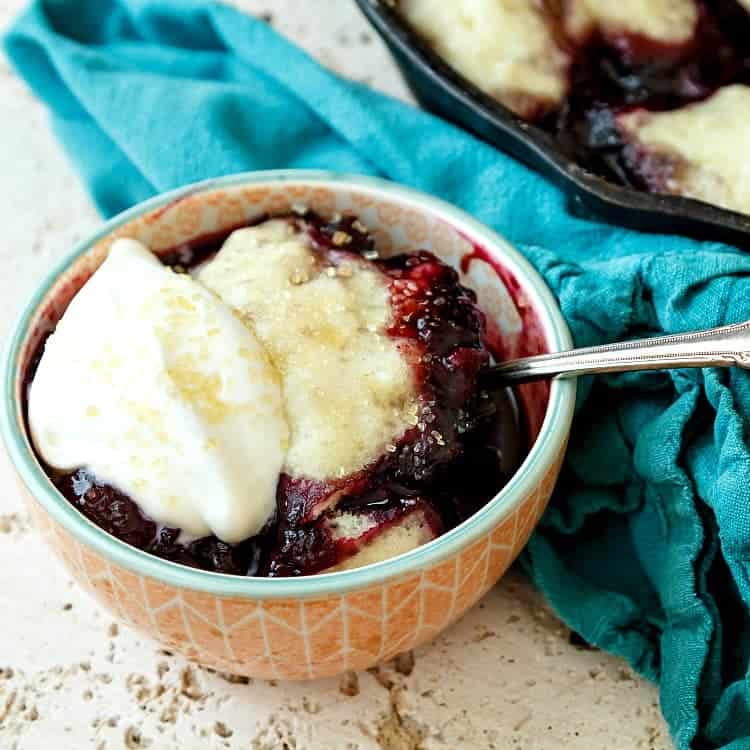 Cherry blueberry slump in a bowl with a spoon and whipped cream.