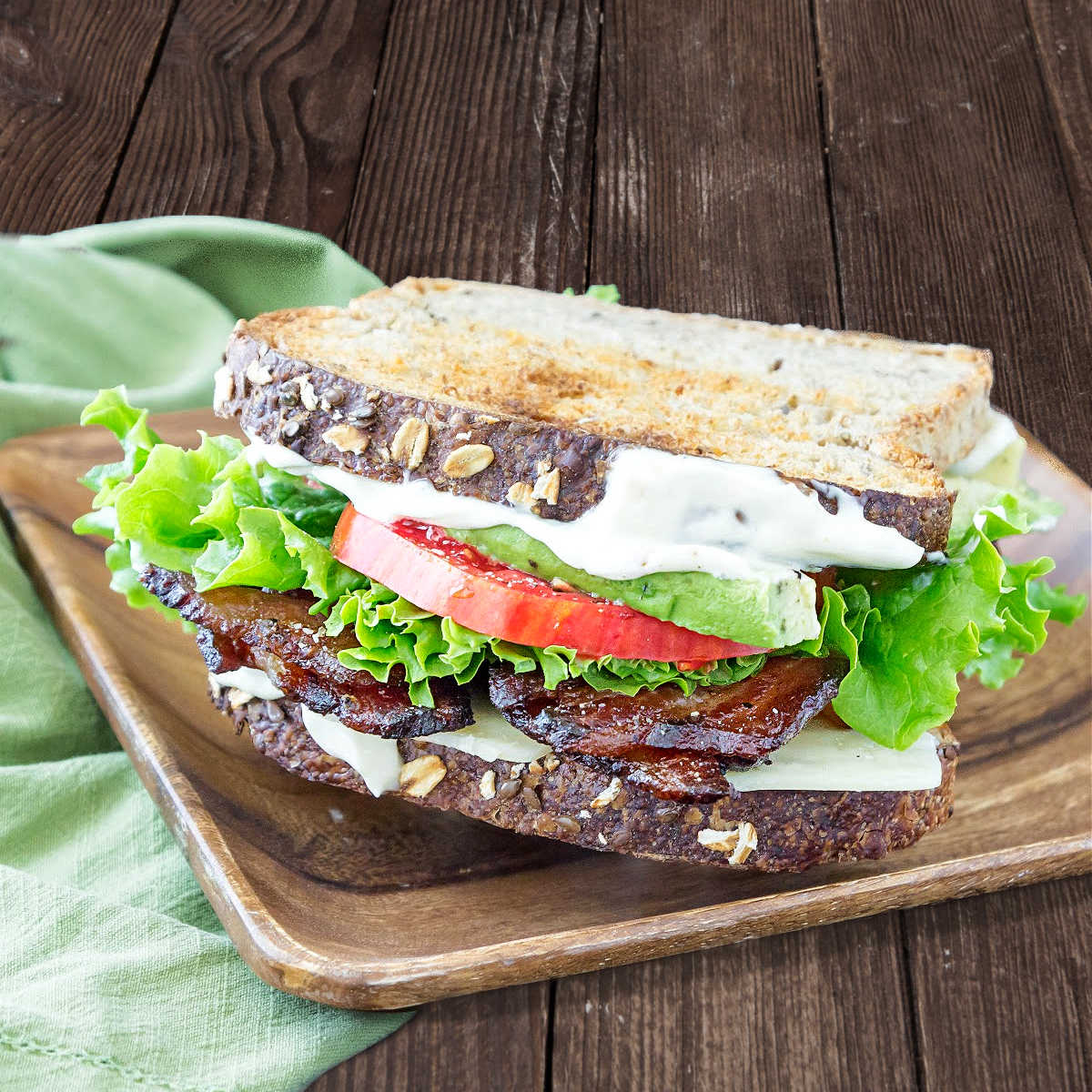 A BLT on toasted multigrain bread on a wooden plate.