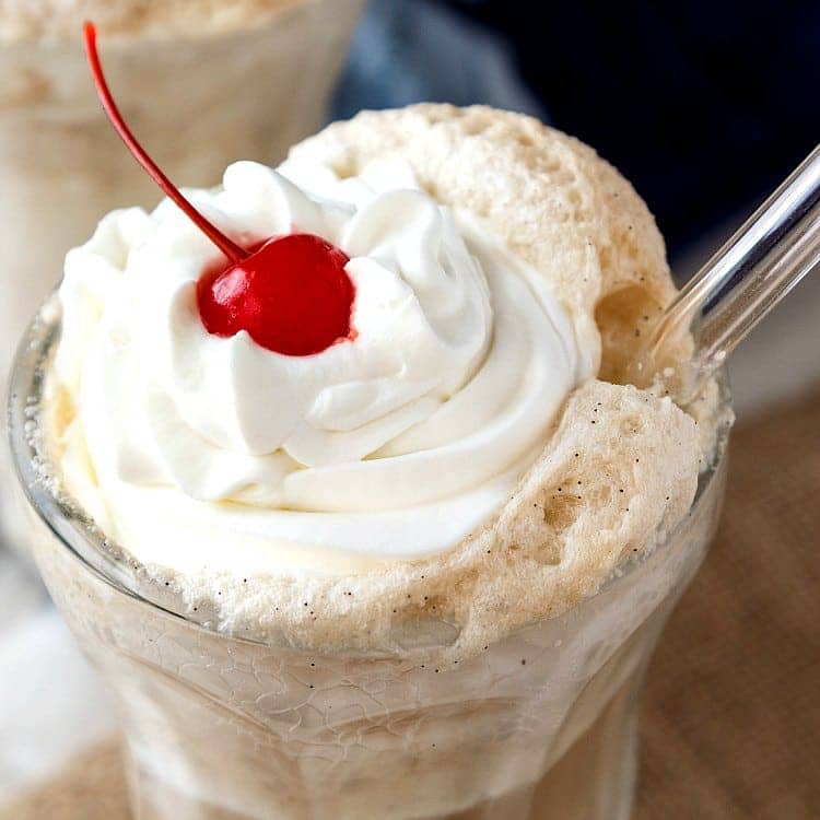 A close up of the top of a root beer float with whipped cream and a cherry.