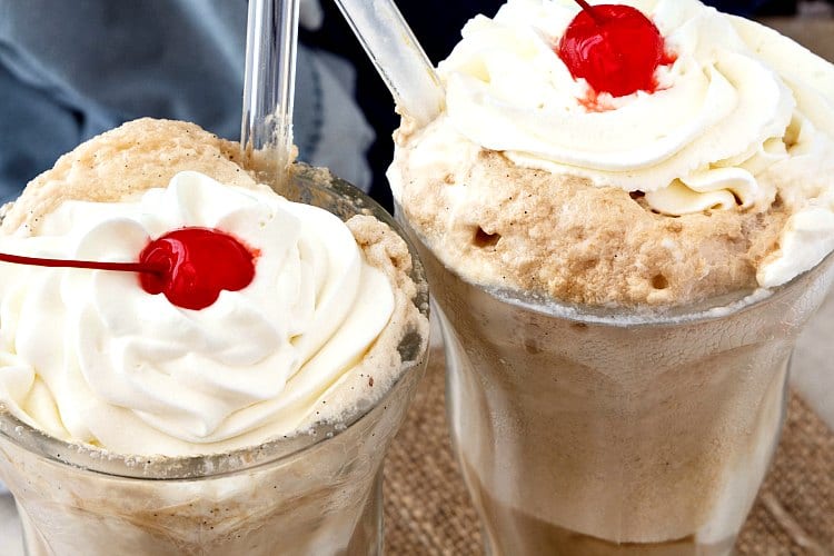 Two root beer floats with whipped cream and cherries on top.