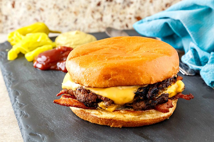 A double smashed burger on a piece of slate with condiments in the background.