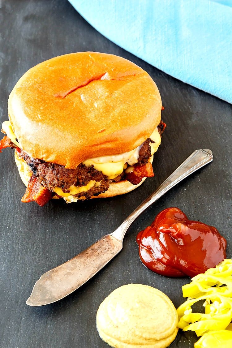 A smashed bacon double cheeseburger on a slate with mustard, ketchup, and pepperoncini.