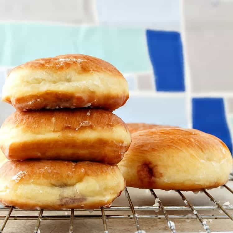 A stack of 3 yeast-raised doughnuts on a cooling rack.