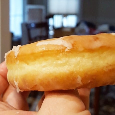 Close up side view of a fried and glazed doughnuts showing a pale strip around the center.