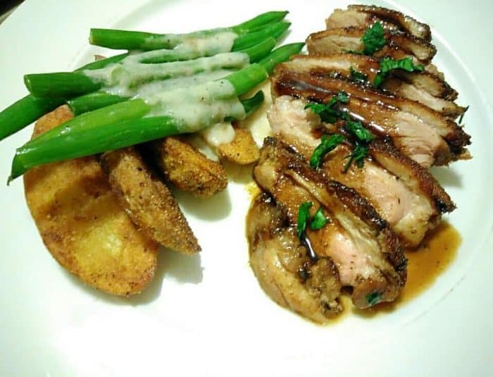 Seared Peking Duck with fingerling potatoes and haricots verts with a white sauce on a white plate.