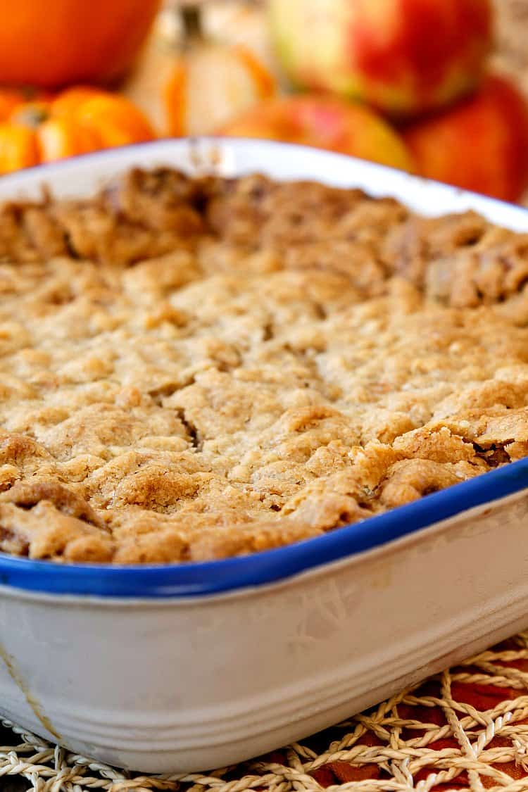 A square baking dish of streusel topped sweet breakfast casserole with apples in the background.