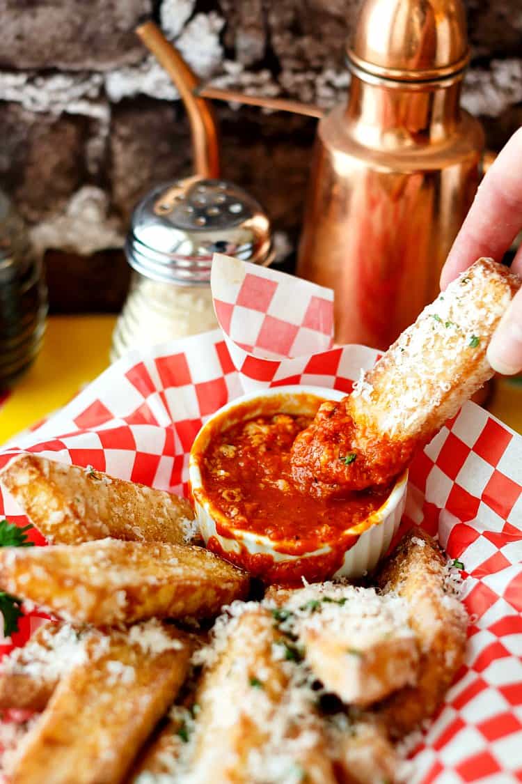 One cheesy polenta fry being dipped into homemade red pepper ketchup.