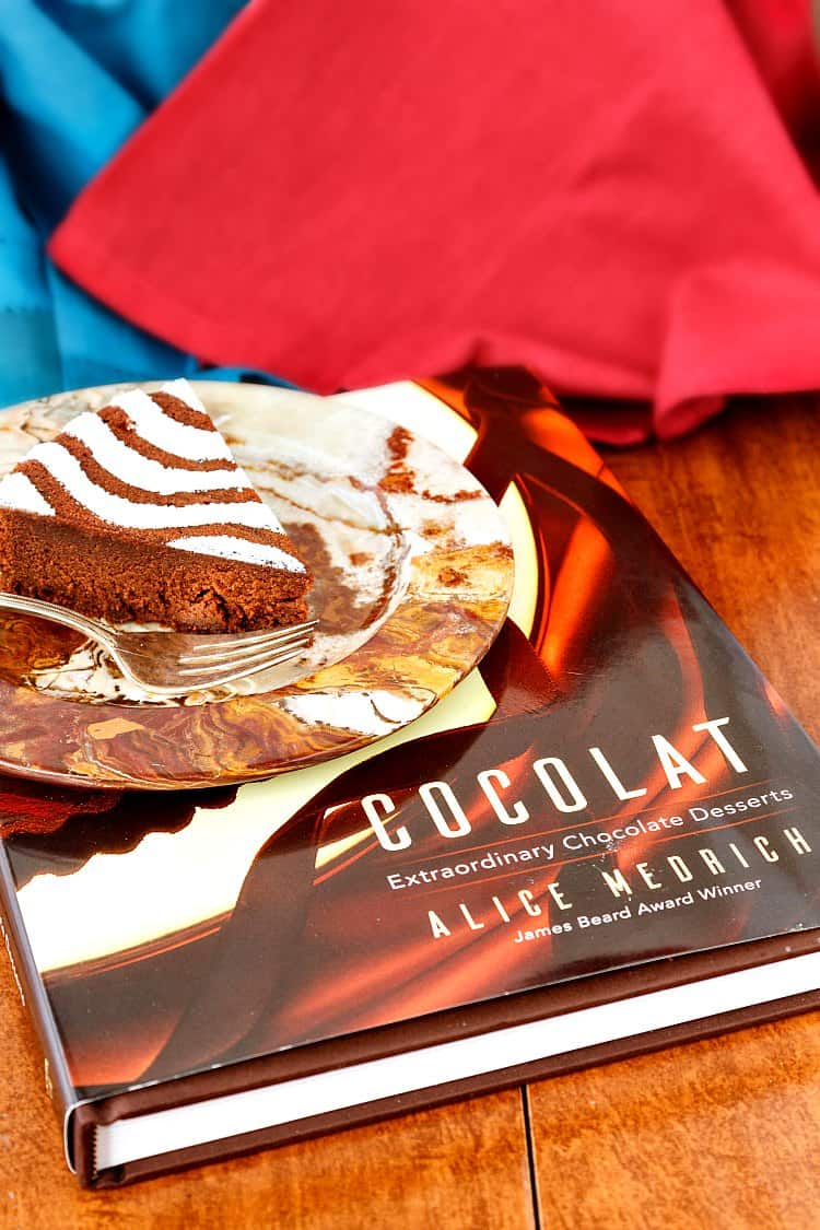 A slice of chocolate torte on a marbled plate on top of the book "Cocolat" by Alice Medrich.