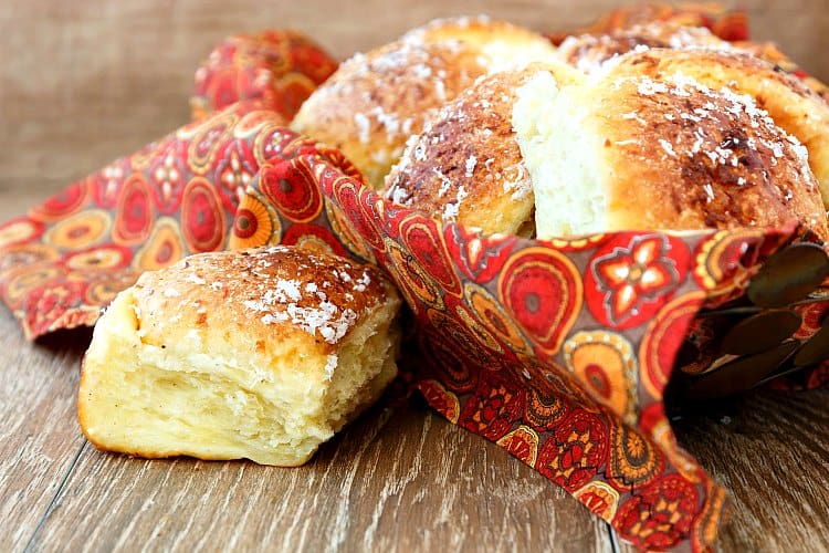 A basket of soft dinner rolls made with garlic and Parmesan cheese on a wooden board.