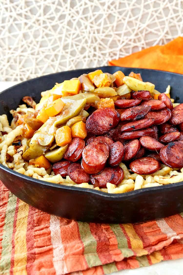 Polish sausage with apples onions and butternut squash over spaetzle in a cast iron pan. 