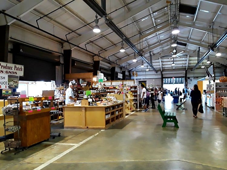State farmers market in Raleigh, NC showing wide view of different vendors in a large hall with high ceilings and concrete floors.