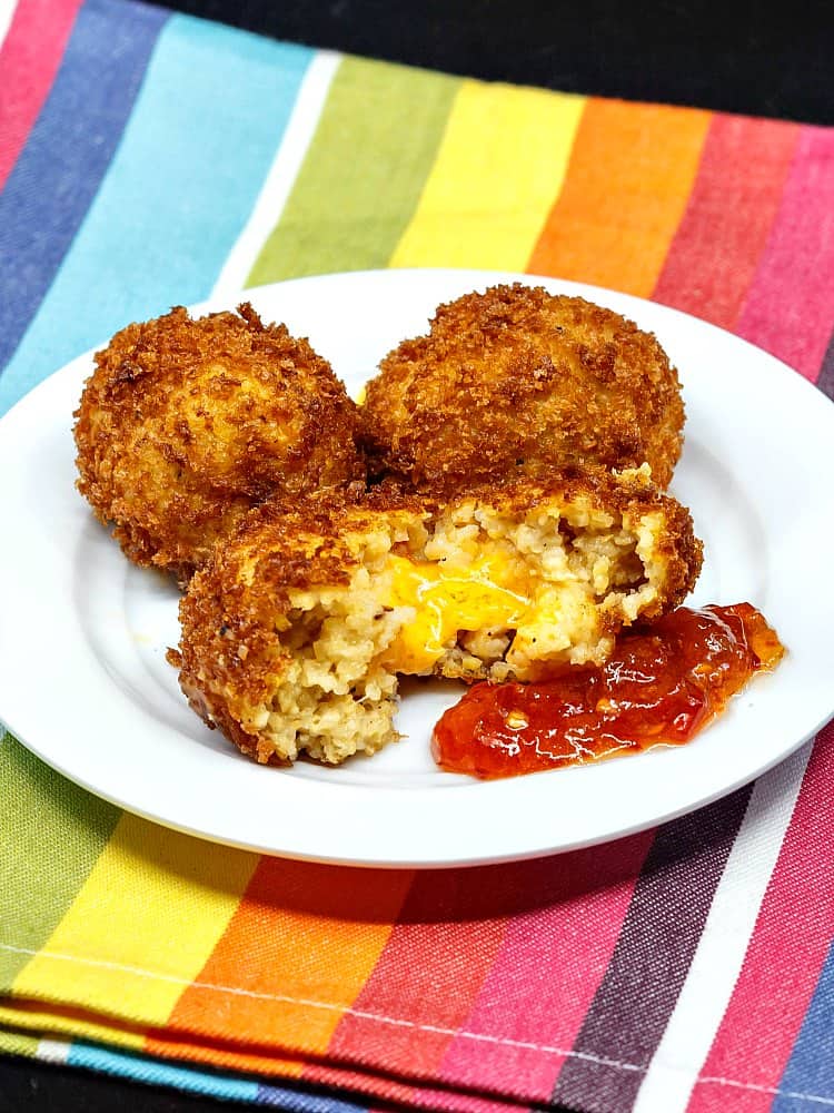 A split open Pimento Cheese Stuffed Grits Arancini with a dollop of pepper jelly. Cheese is oozing out of arancini.