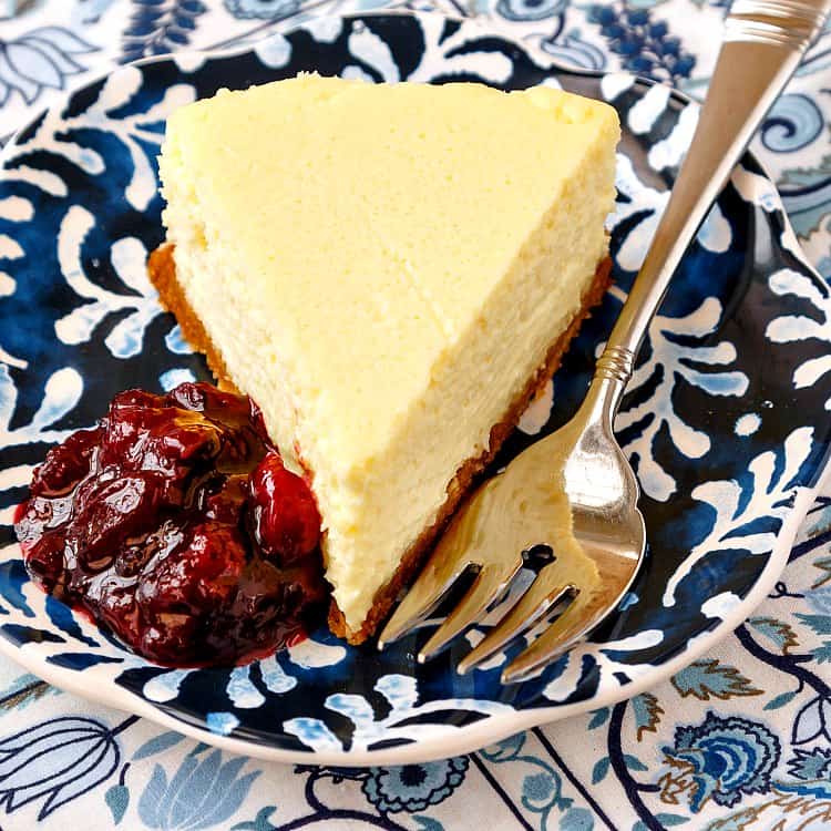 Corn cheesecake slice on a blue and white plate with a fork and fruit compote.