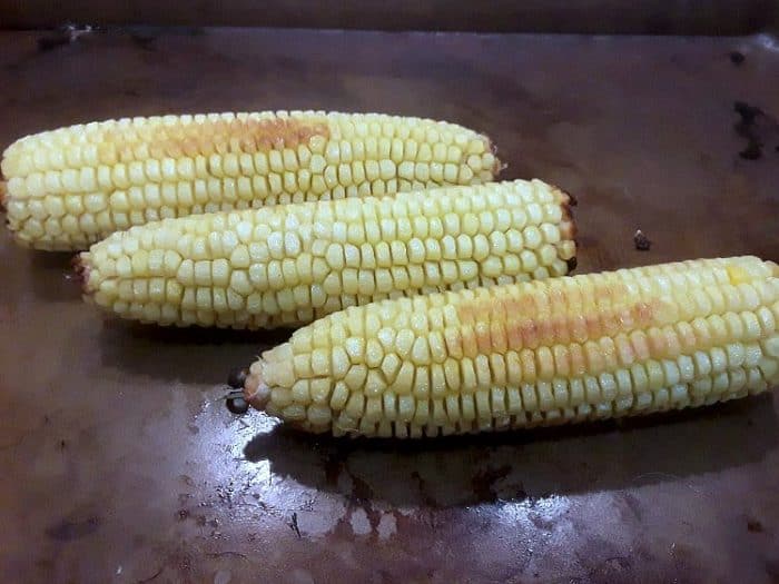 Three ears of corn roasting on a pan in the oven.