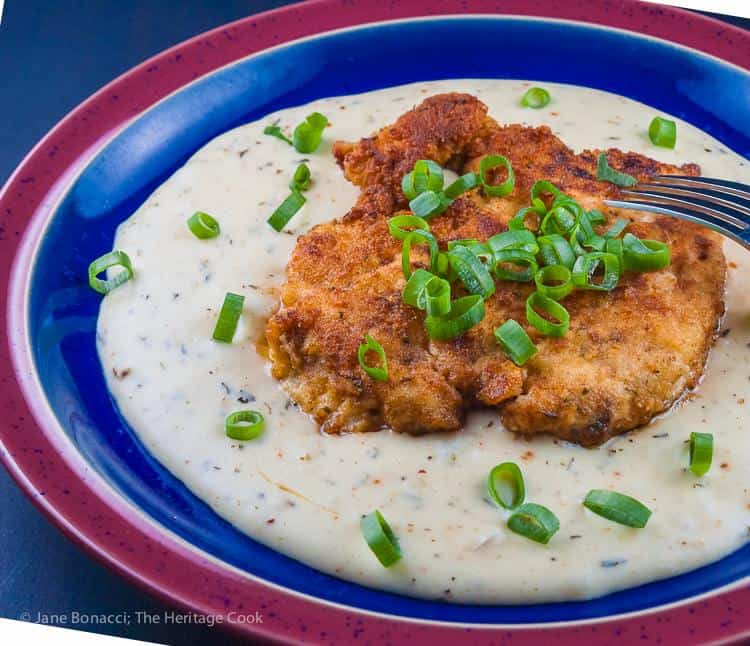 Fried chicken cutlets on a blue and red plate with creamy white herb gravy.
