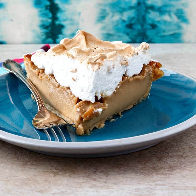 A slice of butterscotch meringue pie on a blue plate.