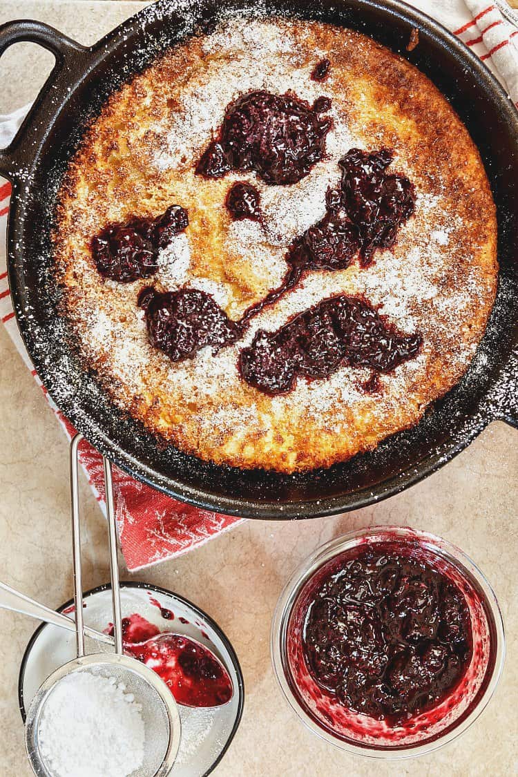 German pancakes baked in a cast iron frying pan topped with preserves and powdered sugar.