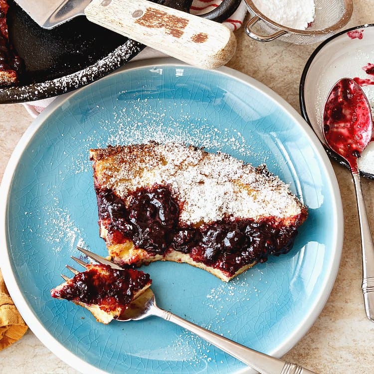 Overhead view of a slice German pancakes made with Idaho® potatoes with several bites taken out and one on a fork ready to eat. All is topped with preserves and powdered sugar. 