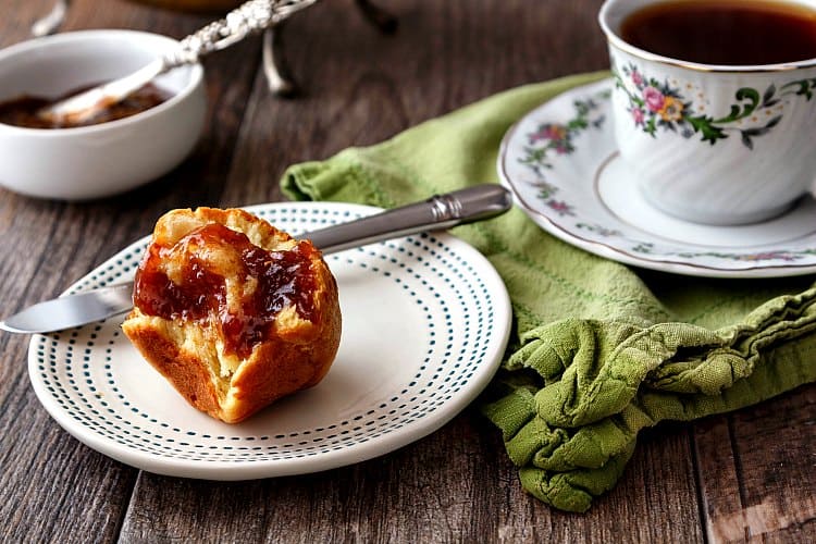 A brioche bun slathered with jam next to a cup of coffee. 