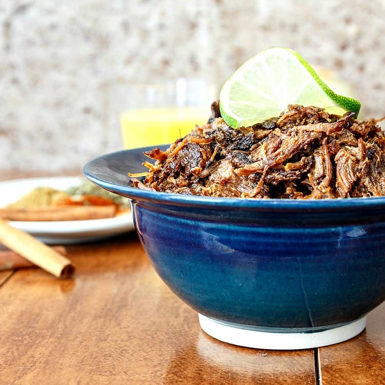 Beef carnitas made in an instant pot and piled into a blue bowl with a lime garnish.