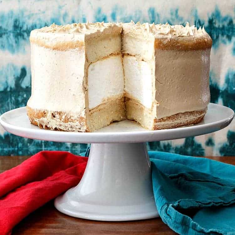 Peanut butter marshmallow cake on pedestal with one slice cut out of it.