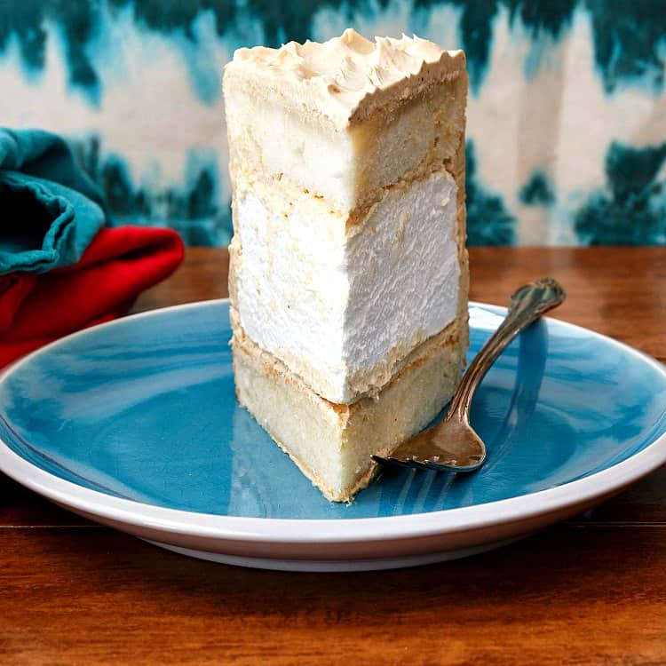 A tall slice of cake on a blue plate, showing the thick marshmallow layer in the middle.