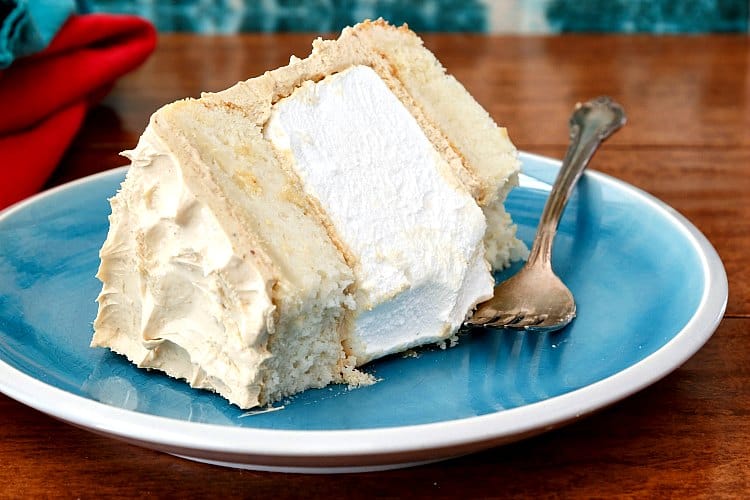 A slice of white cake layered with marshmallow and peanut butter Swiss meringue buttercream on a plate with a bite taken out of one corner.