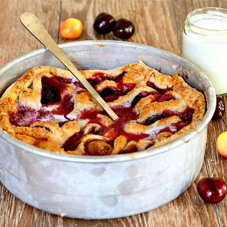 A deep round aluminum pan filled with baked cherries and blackberries and covered in a lattice-type crust.