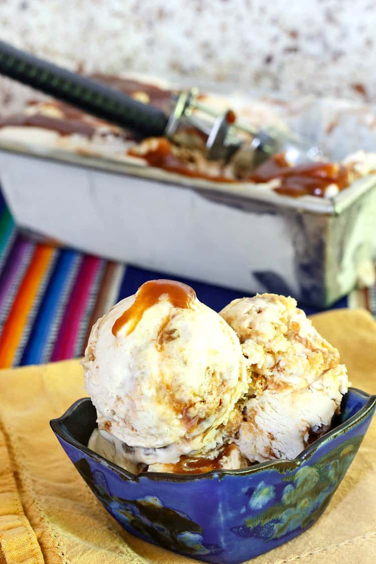A blue bowl of ice cream with caramel swirls and bits of cinnamon roll with the container of ice cream in the background.
