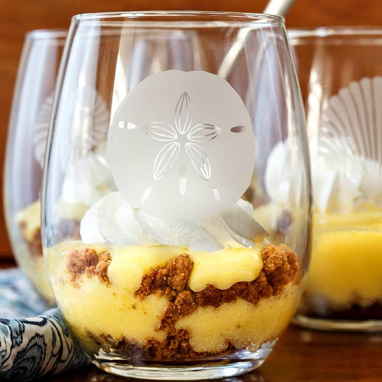Close up shot of key lime pie parfaits in stemless wine glasses with different shells etched on them.