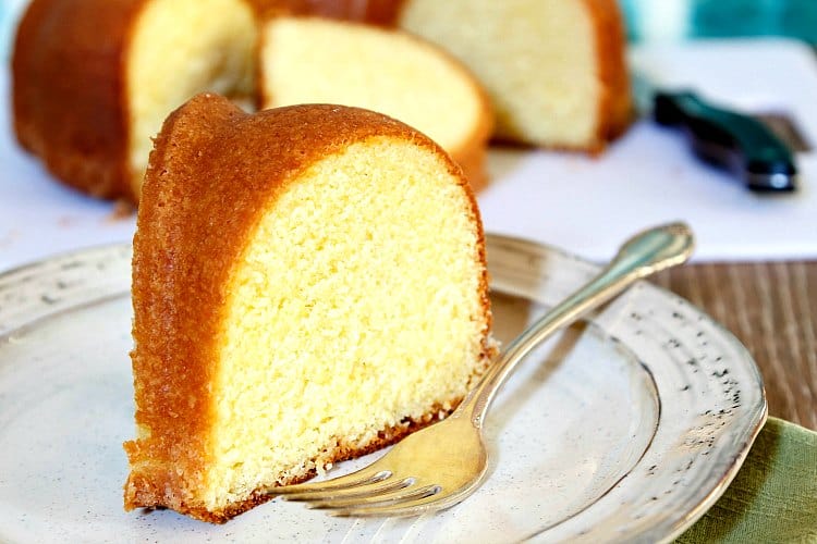 A close up shot of slice of buttermilk pound cake on a plate with the sliced cake and a knife in the background.