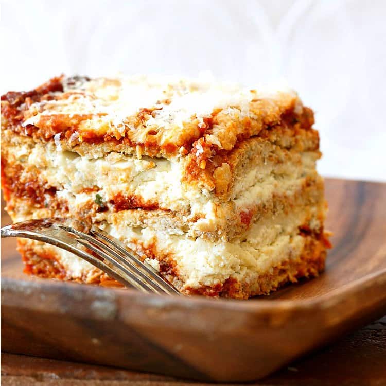 A slice of lasagna made with cauliflower pasta noodles on a wooden plate.