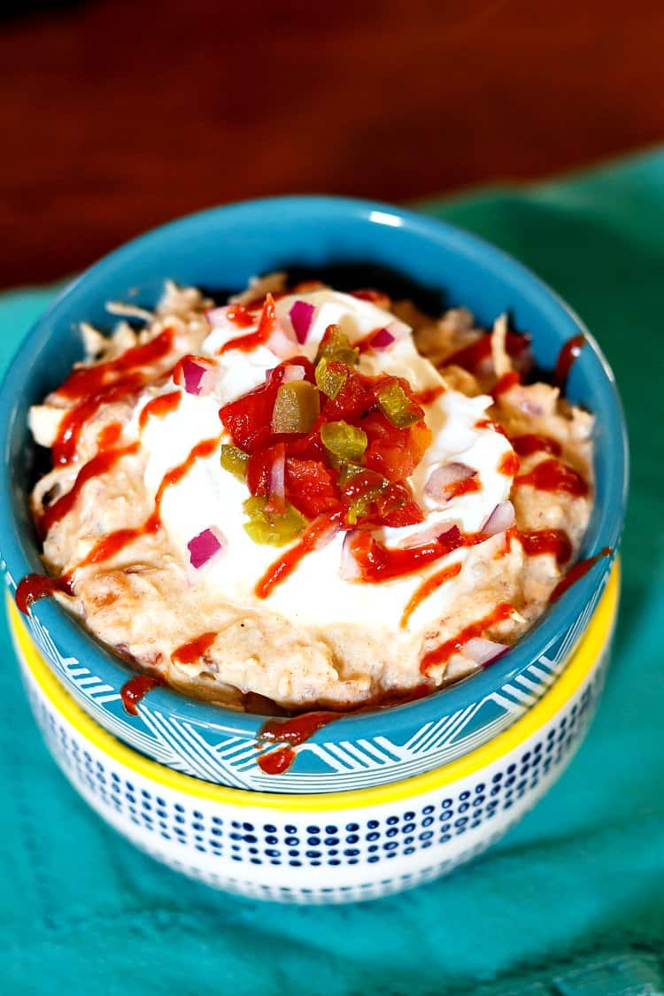 Overhead shot of creamy chicken in a blue bowl topped with sour cream, minced tomato and pickled pepper,and a zigzag of hot sauce.