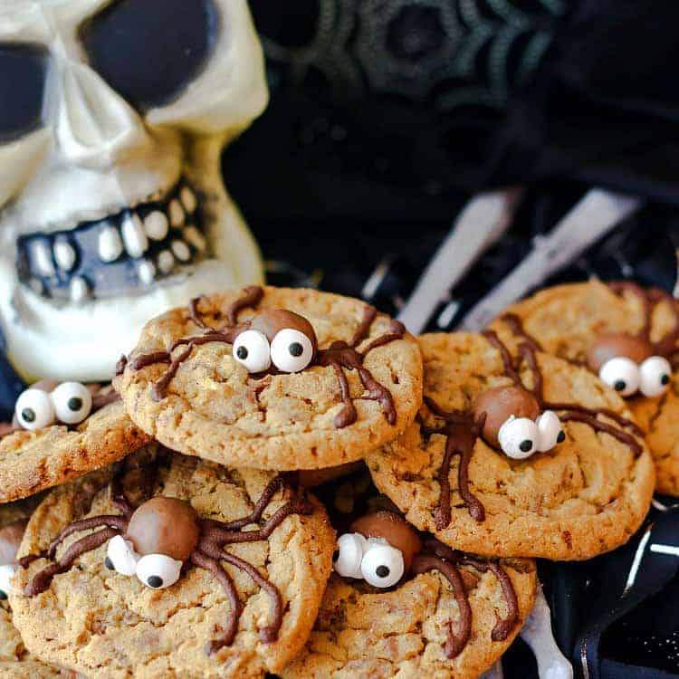 A pile if malted milk ball spider cookies on a plate with a plastic skull in the background.