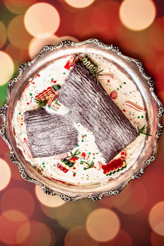 Overhead shot of a yule log cake on a silver platter with whipped cream and old-fashioned hard candy decorating it.