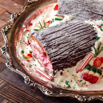 A 3/4, vertical shot of a buche de noel decorated with whipped cream and filled with pink filling on a silver platter.