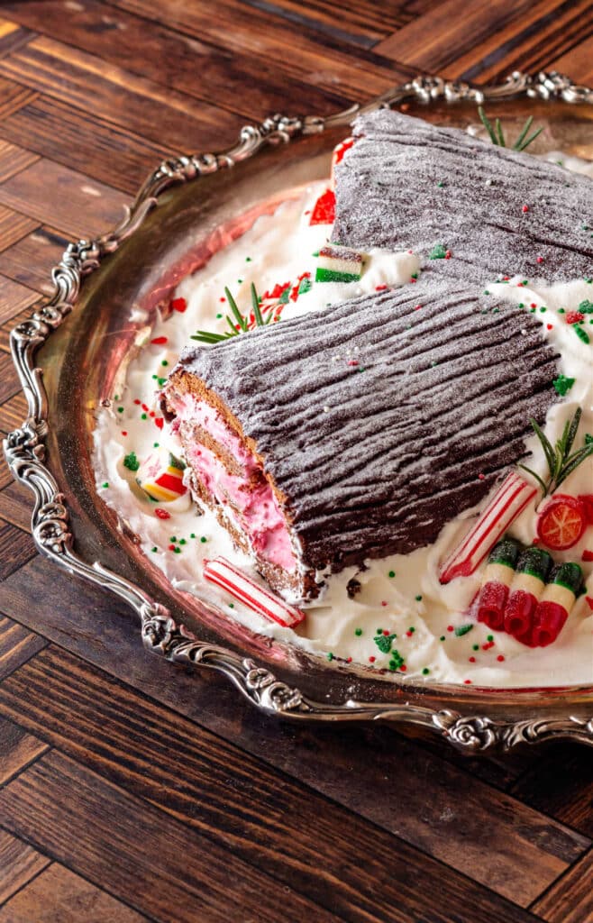 A 3/4, vertical shot of a buche de noel decorated with whipped cream and filled with pink filling on a silver platter.
