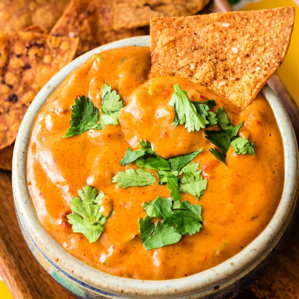 Overhead shot of spicy chili cheese dip in a bowl with a tortilla chip in it.