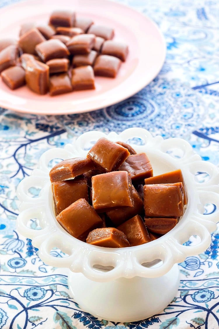 Square pieces of butterscotch candy in a white footed candy dish and another pile of candy on a pink plate.