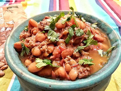 close up of soupy pinto beans in a blue bowl topped with chopped cilantro