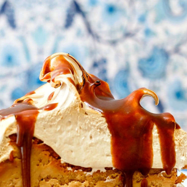 Thick brown sugar meringue on top of a  slice of gluten-free cheesecake with butterscotch sauce.