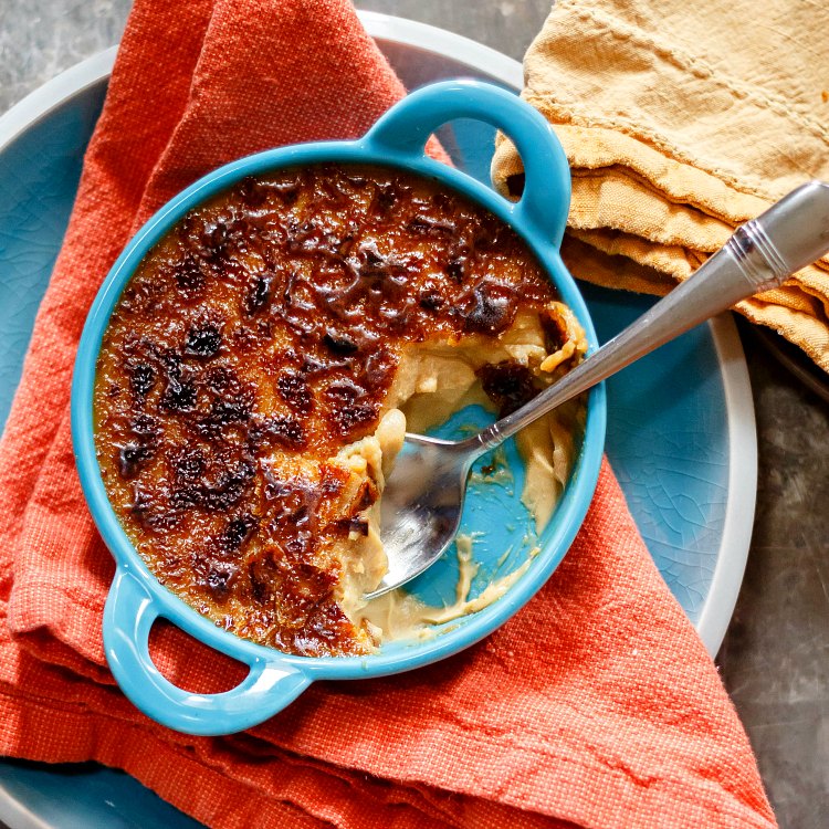 Overhead shot of butterscotch creme brulee in a blue ramekin, partly eaten with a spoon in it.