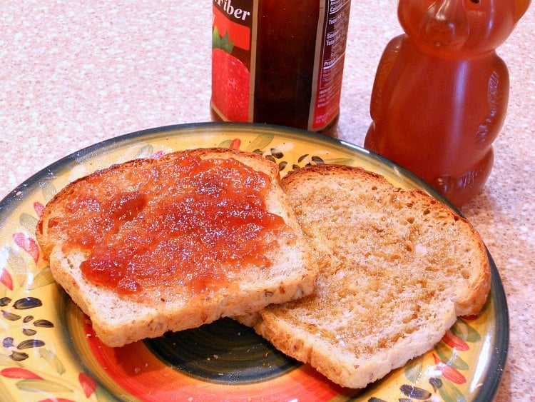 Two toasted pieces of bread, one with honey drizzled on it and one with jam, on a plate.
