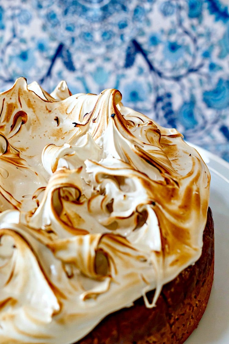 A whole gluten-free butterscotch cheesecake on a white cake stand with lots of browned meringue on top.