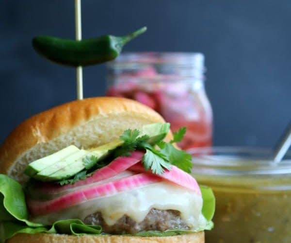burger on a cutting board with a roasted chile skewered through the center