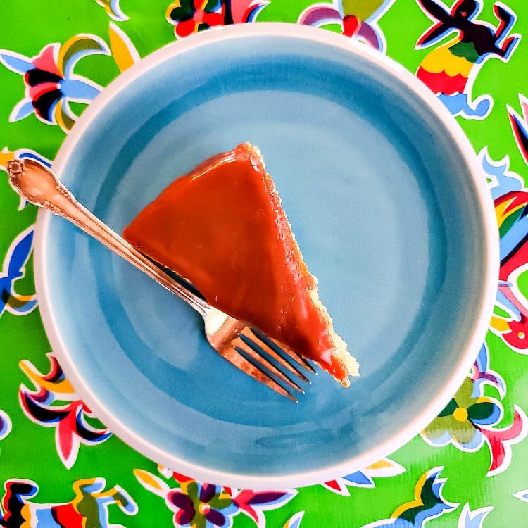 Overhead shot of an upright slice of cake with butterscotch glaze on a blue plate with a fork.